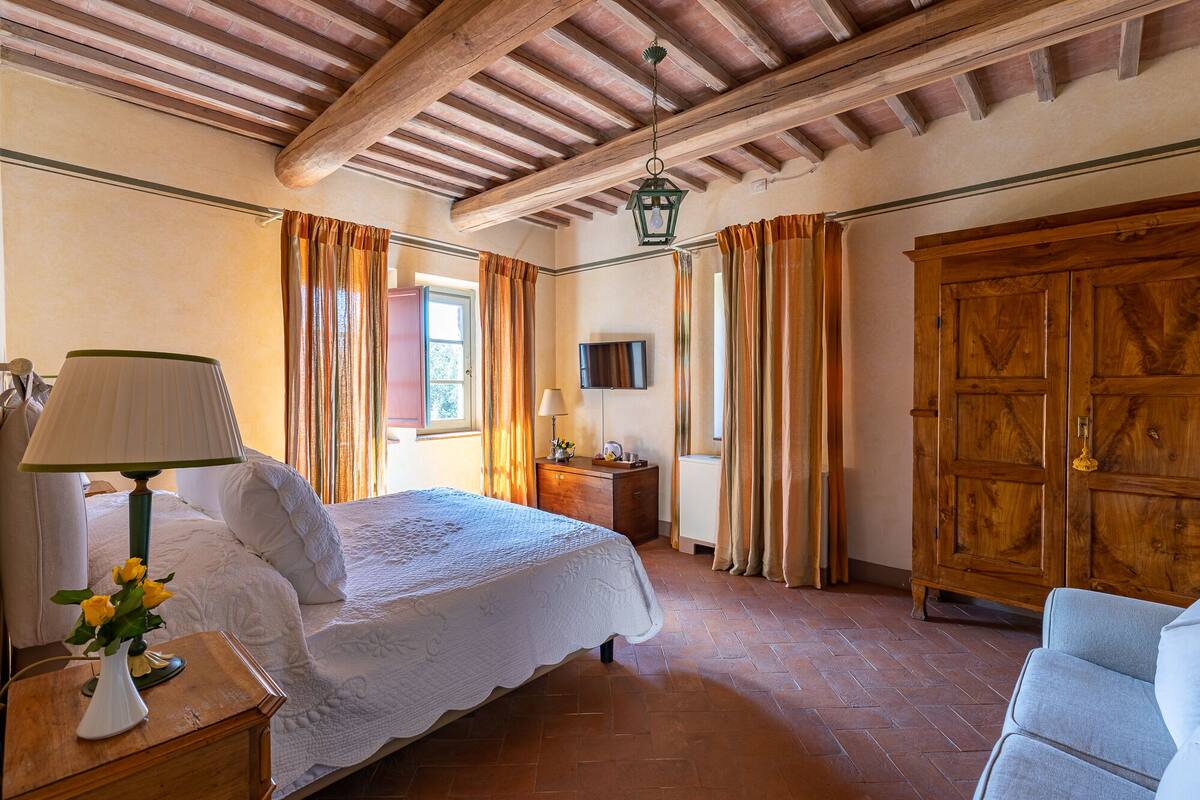 A bedroom with a bed, a nightstand, a lamp, a dresser, a television, and a wooden wardrobe.
