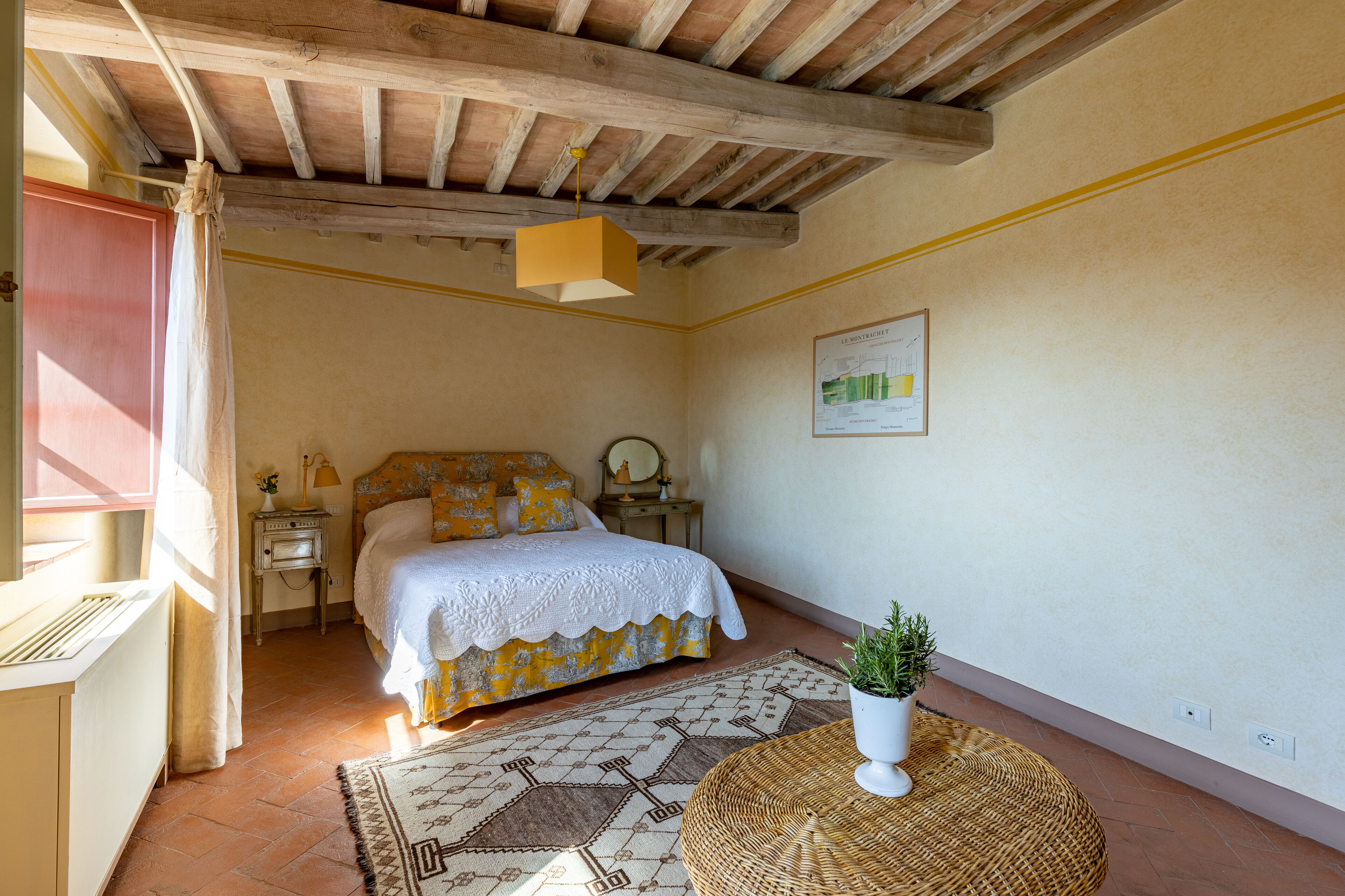 A bedroom with a bed, bedside table, lamp, and a potted plant.