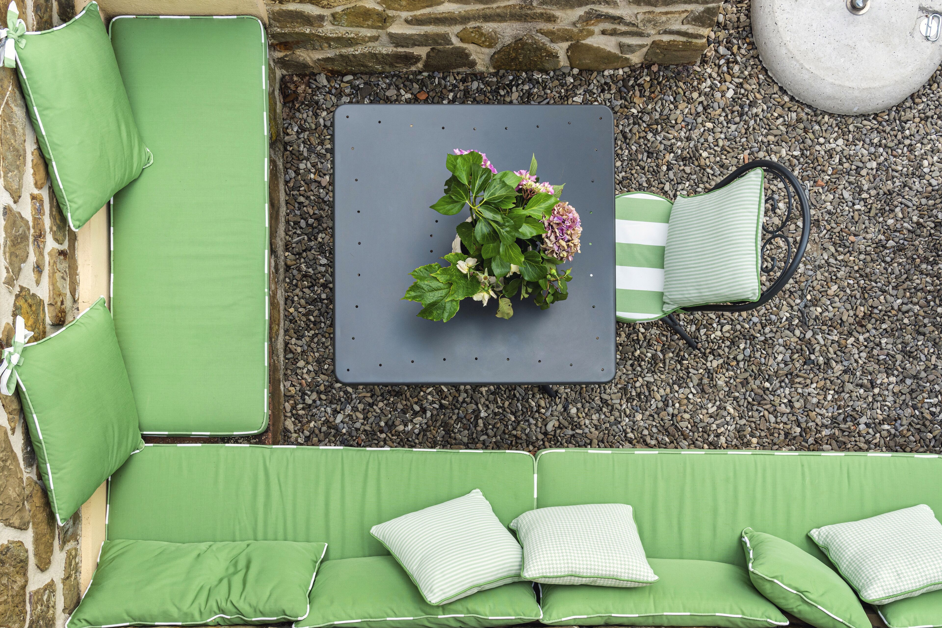 Ein grüner Sitzbereich im Freien mit Tisch, Kissen und einem Blumentopf mit Blumen.