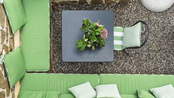 Ein grüner Sitzbereich im Freien mit Tisch, Kissen und einem Blumentopf mit Blumen.