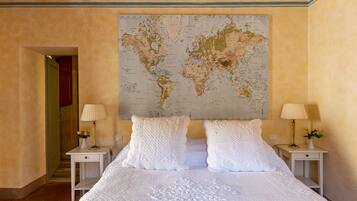 A bedroom with a large world map on the wall, a bed with white linens, two bedside tables with lamps, and a door leading to another room.