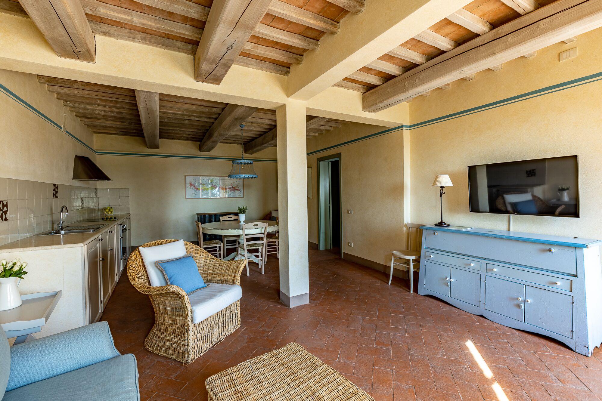 Un amplio salón con una mesa de comedor, mobiliario de mimbre, un televisor y una zona de cocina con lavaplatos y armarios.