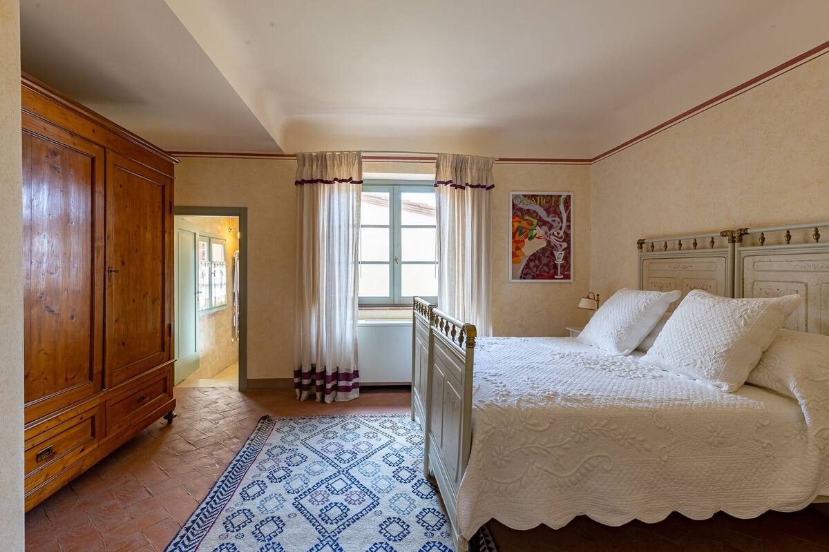 A bedroom with a bed, a wooden wardrobe, a patterned rug, and a window with curtains.