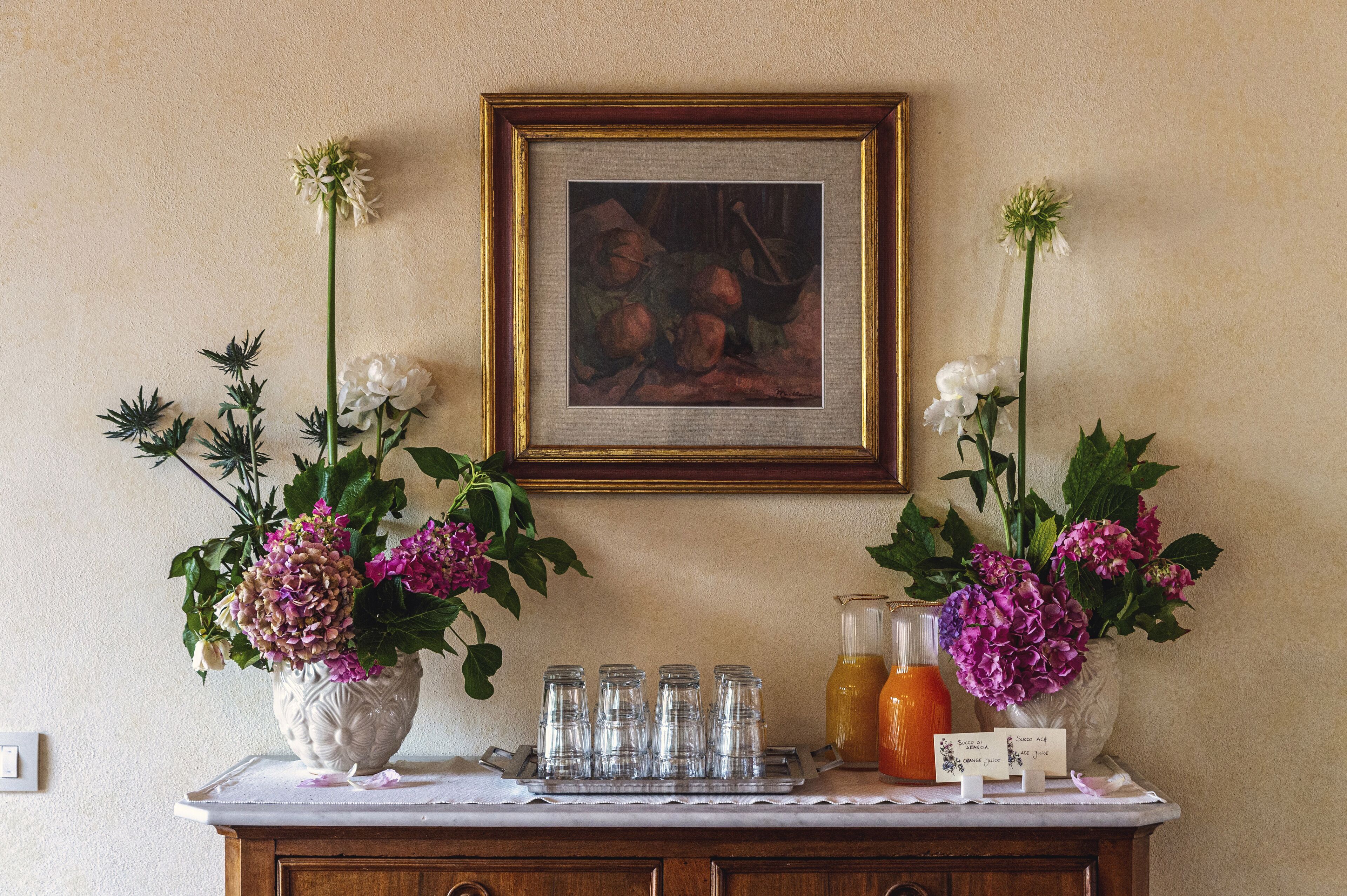 A table with vases of flowers, a framed painting, and a tray of glasses.