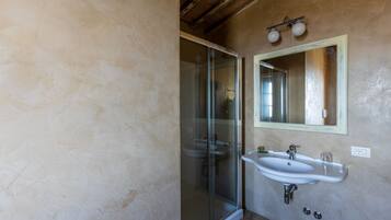 Un baño con cabina de ducha de vidrio, un lavabo blanco y un espejo con luz sobre él.