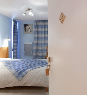 Une chambre à coucher comprenant un lit, une table de chevet, un radiateur fixé au mur et un luminaire au plafond.