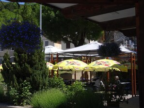 An outdoor seating area with yellow umbrellas, a tree, and a stone building in the background. - Hotel Les Alpins (Saint-Julien-en-Beauchene)