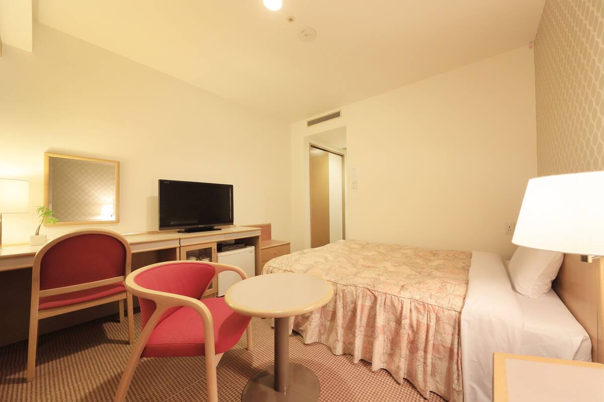 Une chambre d’hôtel équipée d’un lit, d’un bureau, d’une chaise, d’une télévision et d’une petite table.