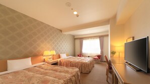 Ein Hotelzimmer mit zwei Betten, einem Fernseher, einem Schreibtisch und einem Vorhangfenster.