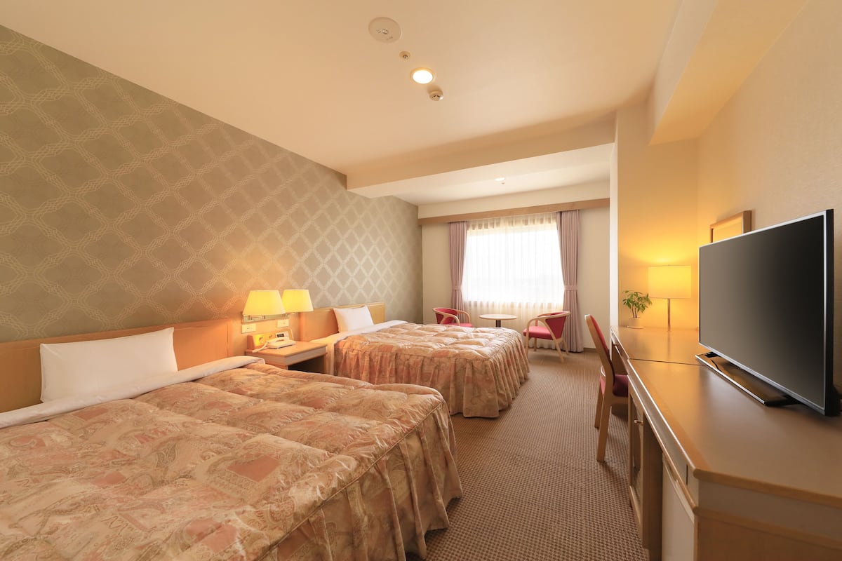 Une chambre d’hôtel avec deux lits, une télévision, un bureau et une fenêtre avec des rideaux.