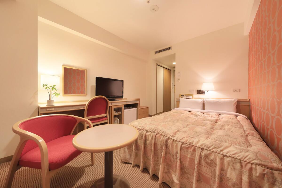 Une chambre d’hôtel comprenant un lit, un bureau avec un ordinateur, une chaise, une petite table et un téléviseur.