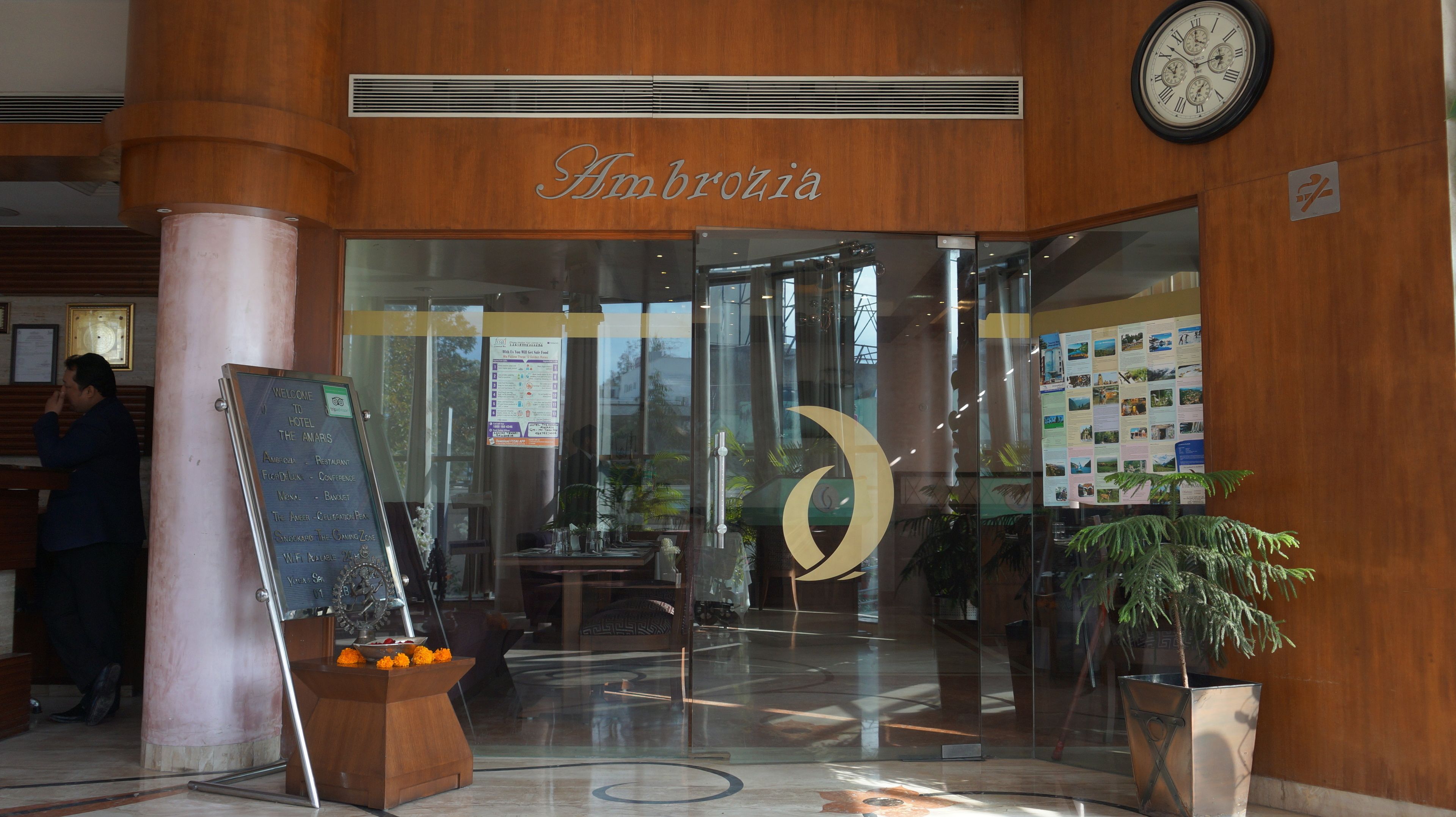 A hotel entrance with a glass door, a clock, and a sign reading "Ambrozia".
