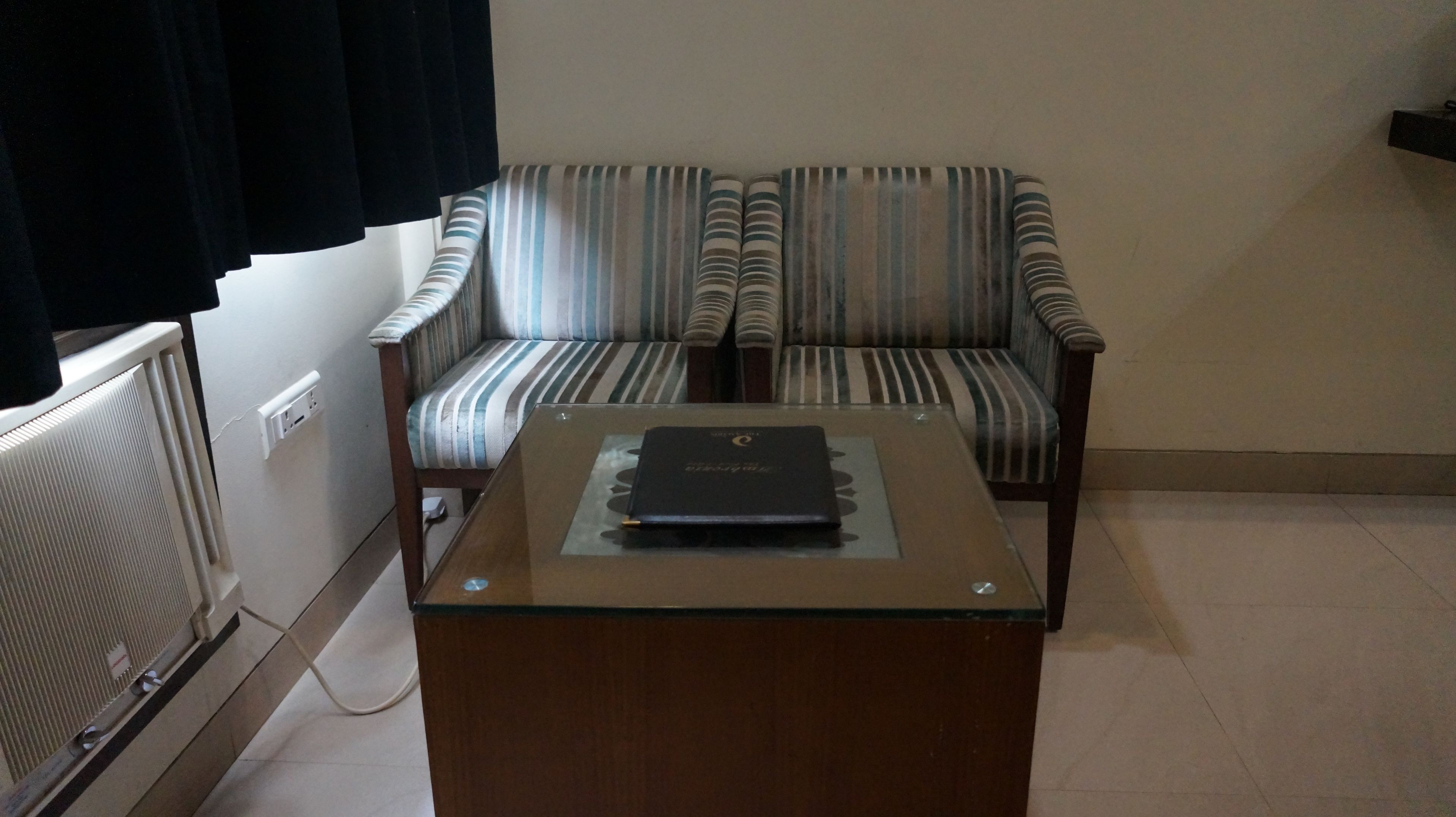 Et værelse med en stribet lænestol, et bord med glasplade og en bog, samt en radiator.