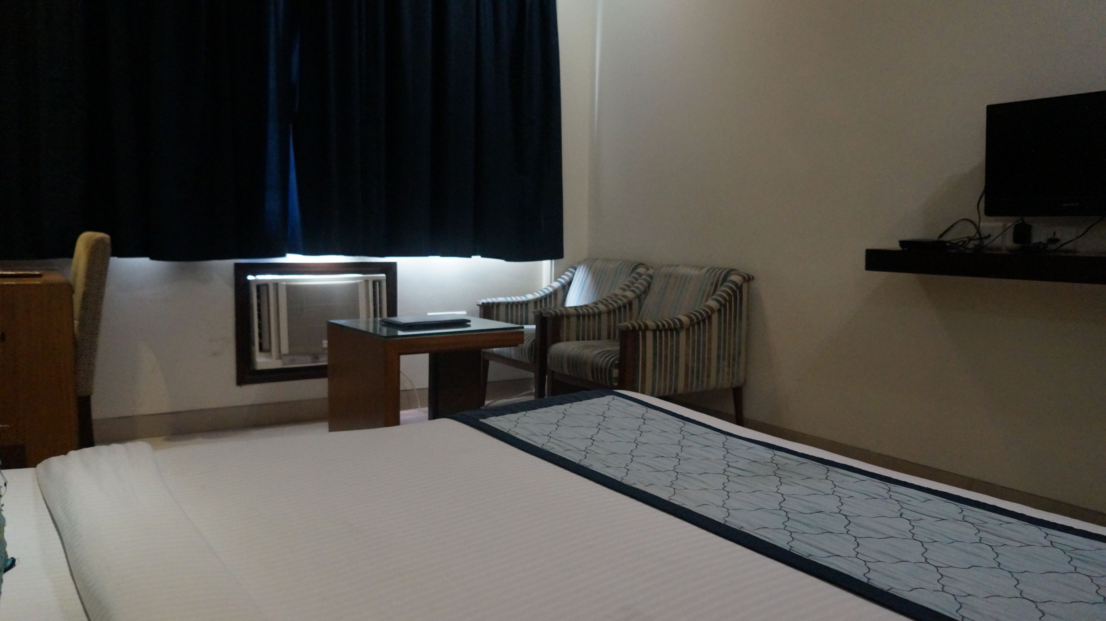 Een hotelkamer met een bed, een bureau, een stoel, een televisie en een raam met gordijnen.