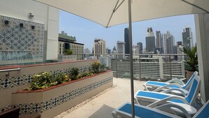 A rooftop terrace with a tiled floor, a large umbrella, and lounge chairs.