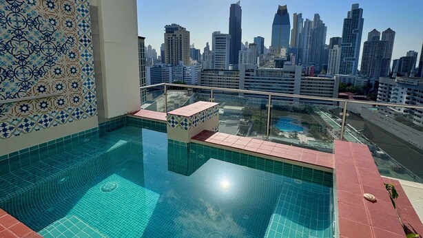 A rooftop pool with a city skyline view, tiled walls, and a clear sky.