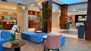 A modern hotel lobby with seating areas, a reception desk, and a garden sign.