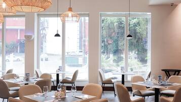 Interior de un restaurante con varias mesas y sillas, amplias ventanas con vistas al exterior e iluminación colgante.