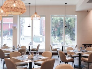 Interior de un restaurante con varias mesas y sillas, amplias ventanas con vistas al exterior e iluminación colgante.