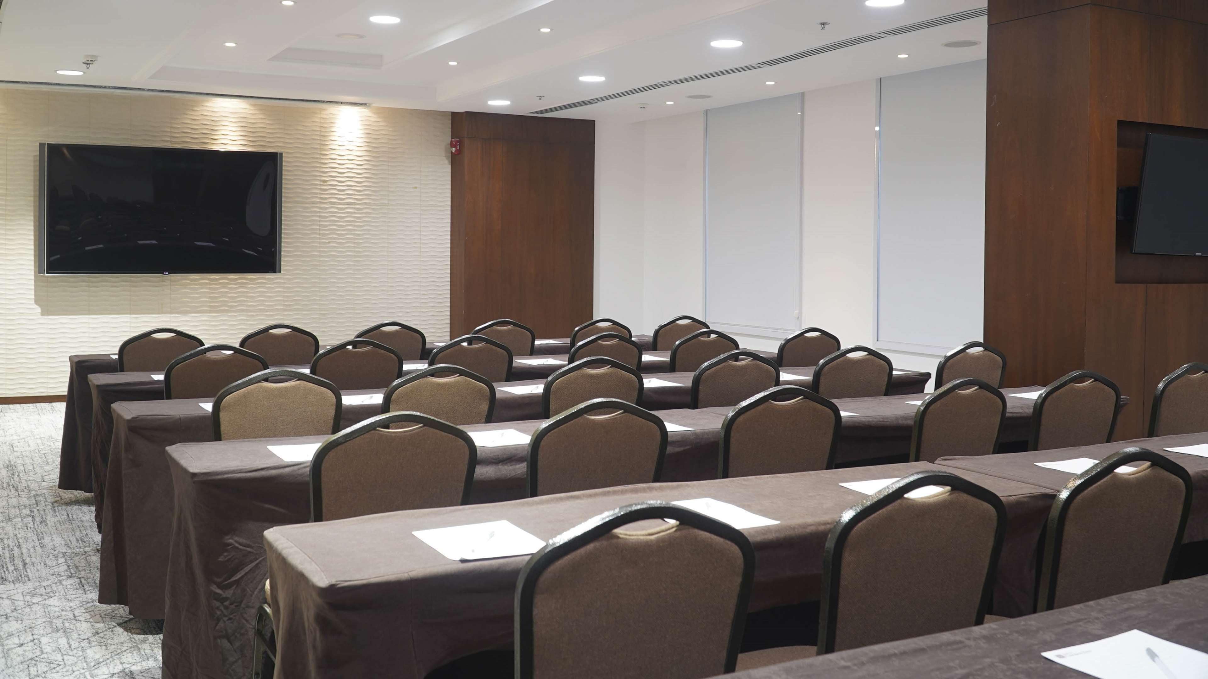 A conference room with rows of tables and chairs, a flat-screen TV, and a whiteboard.