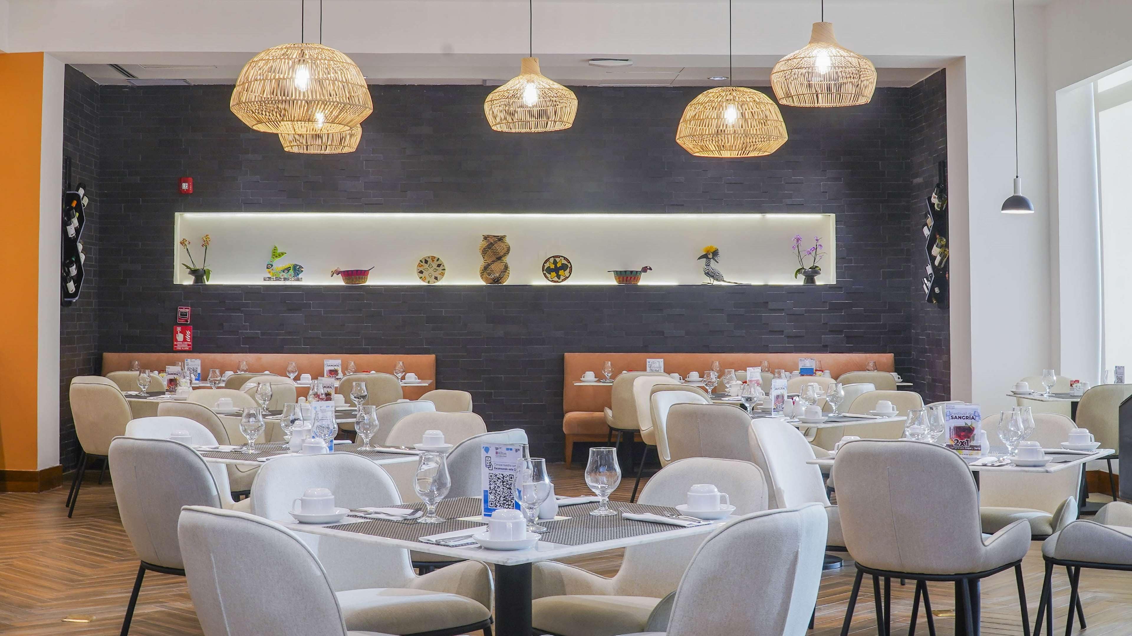 Un restaurante con varias mesas y sillas, estantes decorativos en la pared y lámparas de mimbre colgantes.