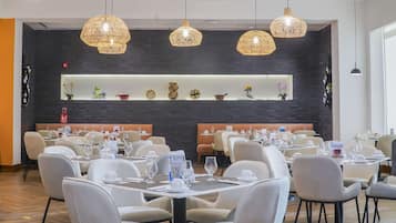 Un restaurante con varias mesas y sillas, estantes decorativos en la pared y lámparas de mimbre colgantes.