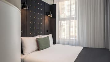 Et moderne hotelværelse med en stor seng, en mørk sengegavl med dekorativ belysning, en senelampe og lette gardiner.