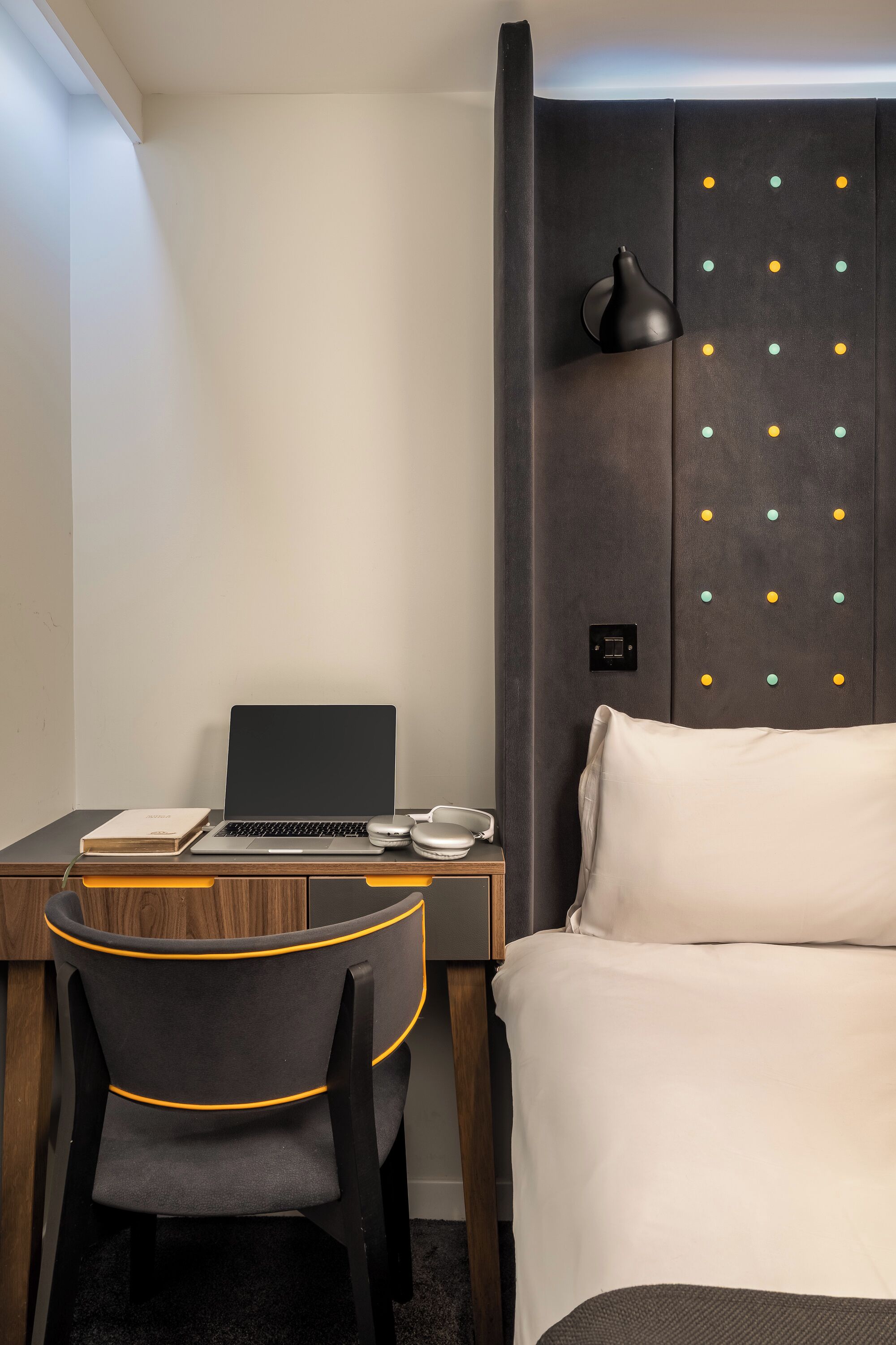 Hotelkamer met een bureau, laptop, stoel, bed en een muur met een opvallend stippatroon.