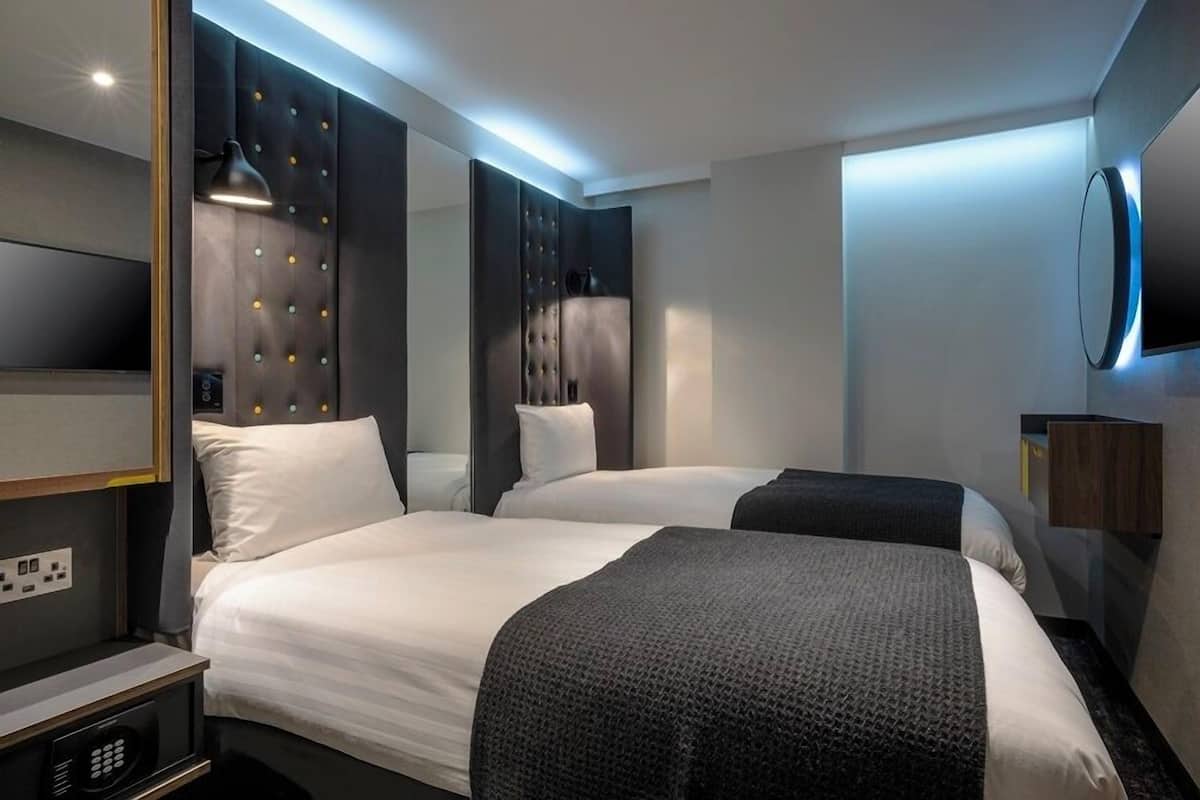 Una habitación de hotel moderna con dos camas, un espejo grande, un televisor de pantalla plana y una mesita de noche con lámpara.