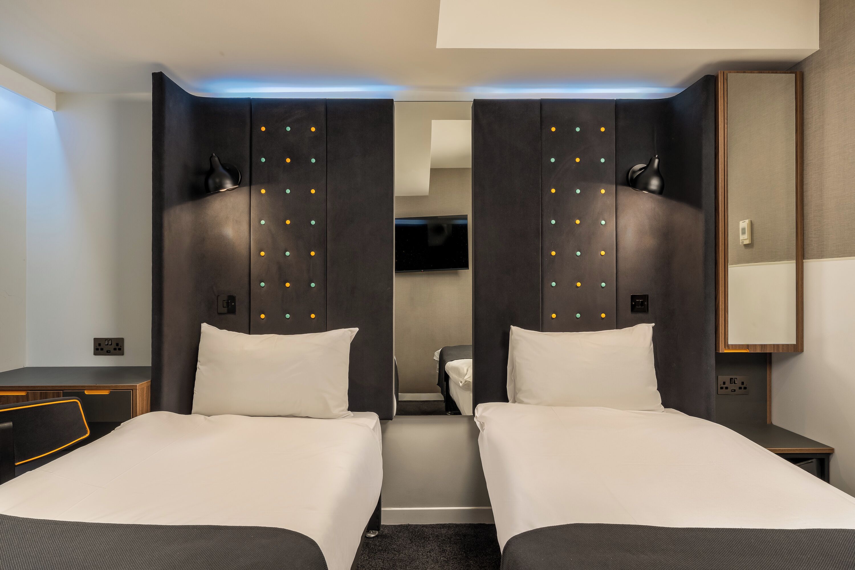 A hotel room with two beds, a desk, a TV, and a mirror.