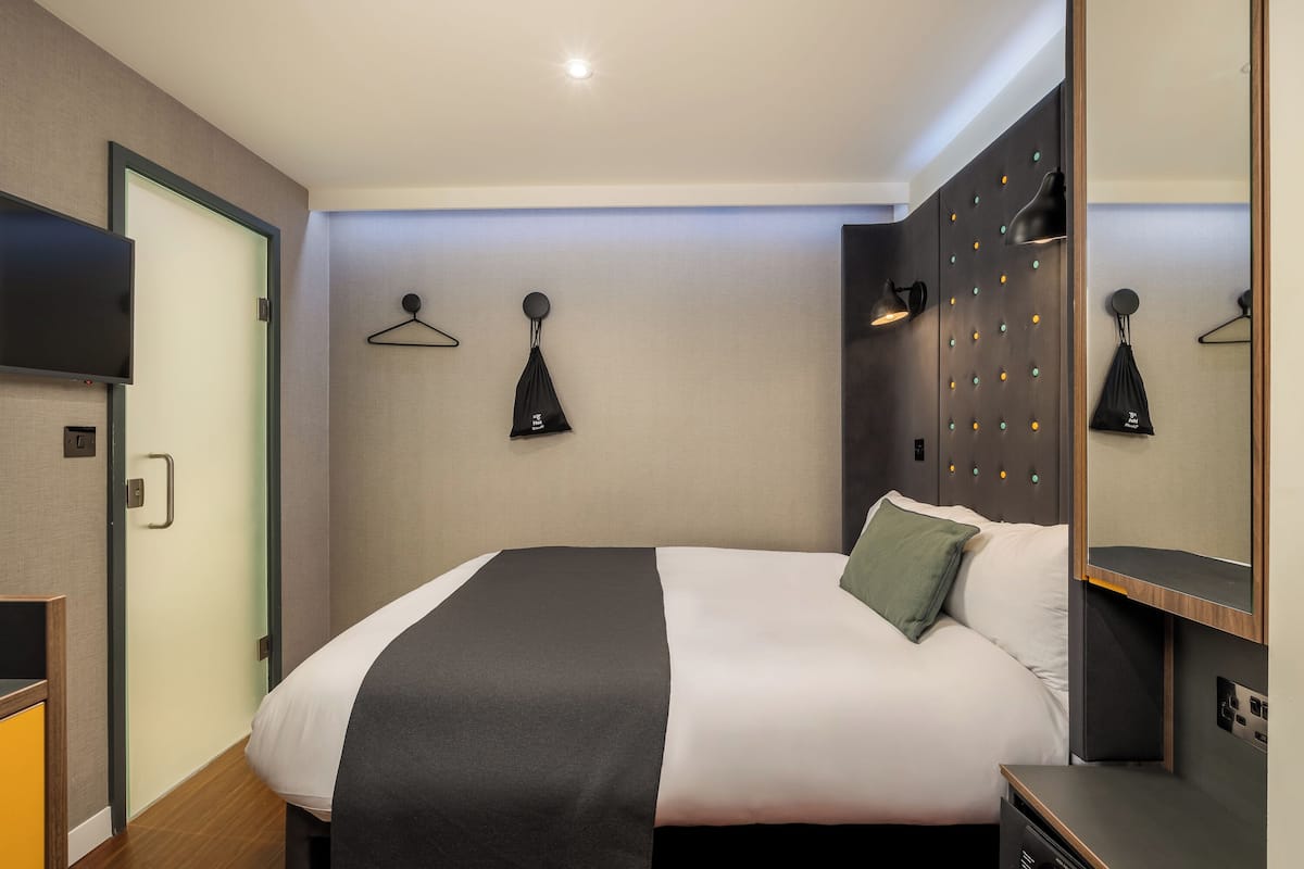 Una habitación de hotel moderna con una cama, un televisor, un armario y un espejo.