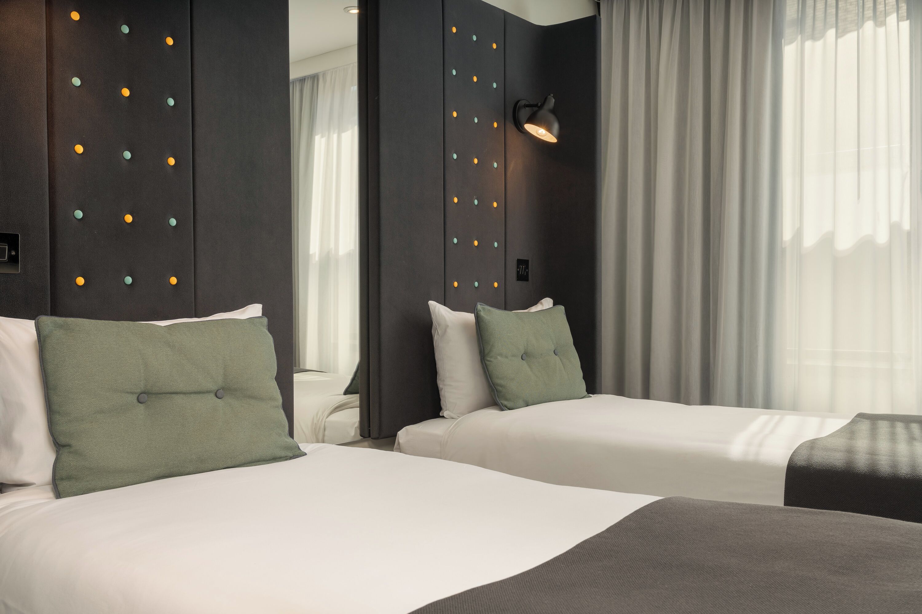A hotel room with two beds, a wall-mounted light, and a window with curtains.