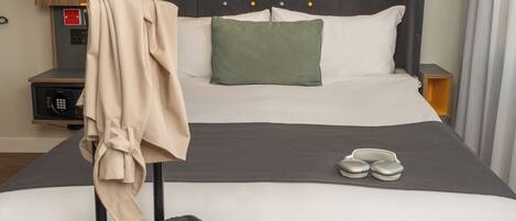 A hotel room with a large bed, a suitcase, and a coat rack.