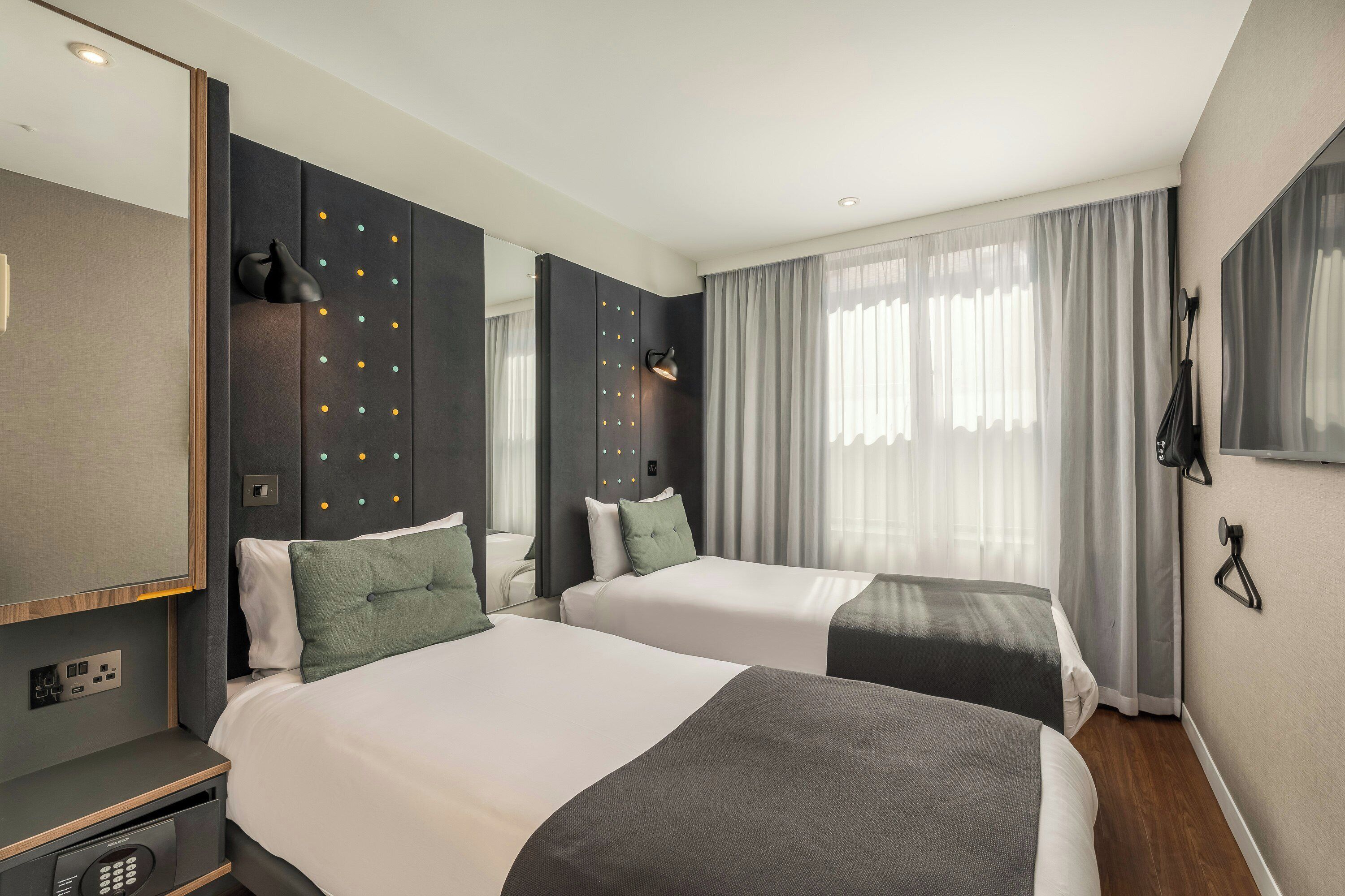 A hotel room with two beds, a large mirror, a wardrobe, and a window with curtains.