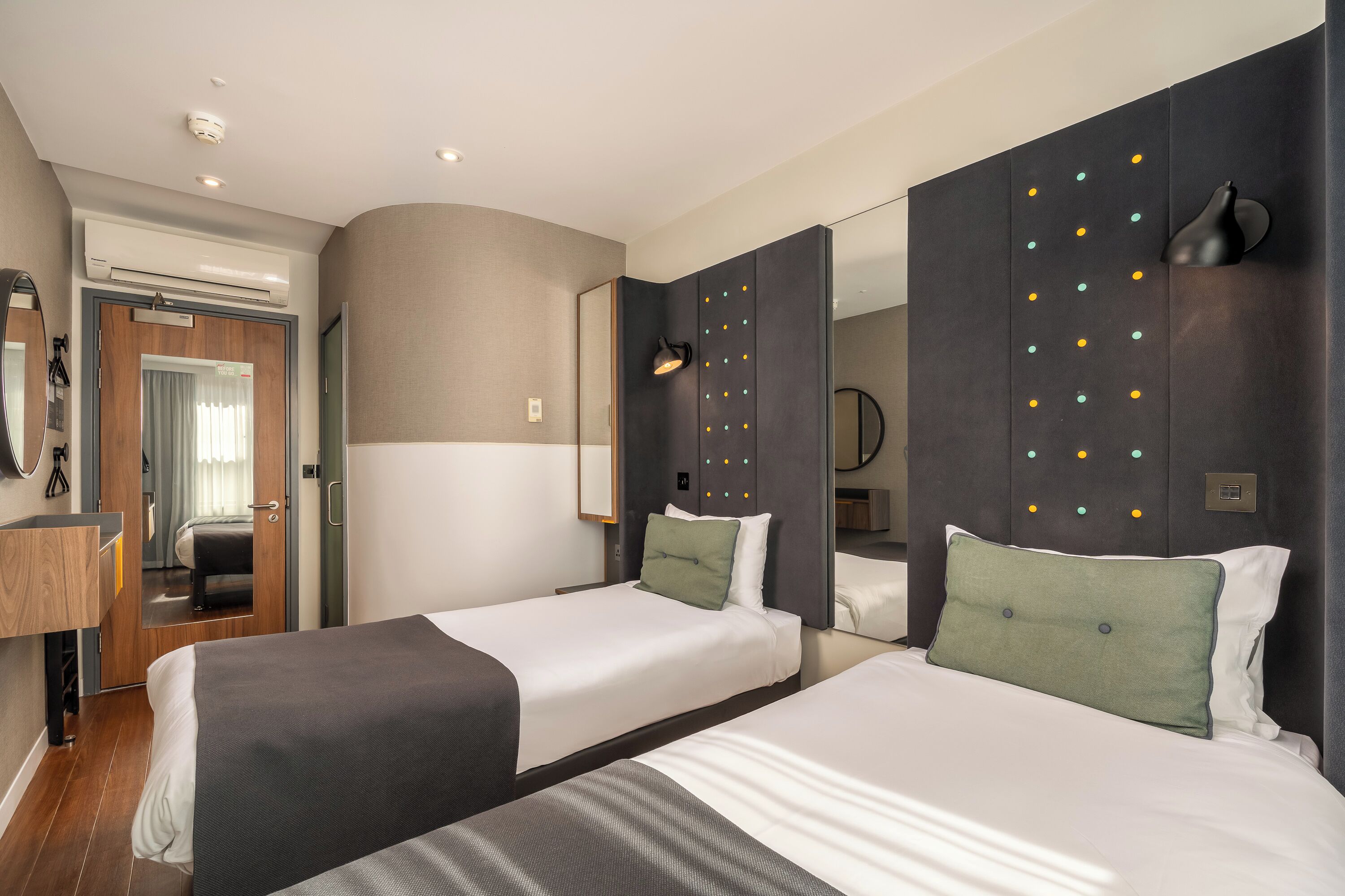 Een hotelkamer met twee bedden, een spiegel, een wandlamp en een airconditioning.