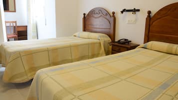 A room with two beds, wooden headboards, a bedside table with a telephone, and a chair.