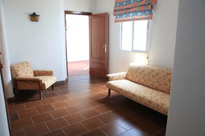 A living room with a sofa and two chairs, a wooden door, and a window with a patterned curtain.