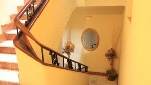 A staircase with a wooden handrail leading to a landing with a mirror and floral decorations. - Hotel El Coloso (Jerez de la Frontera)