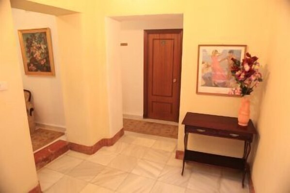 A hallway with a wooden door, a framed painting on the wall, and a small table with a vase of flowers. - Hotel El Coloso (Jerez de la Frontera)