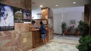 A reception area with marble walls, a reception desk, and a seating area with chairs and a table. - Hotel El Coloso (Jerez de la Frontera)