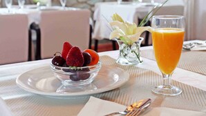 Una escena de desayuno con un bol de fruta, un vaso de zumo de naranja y cubiertos sobre una mesa.