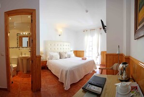 Habitación de hotel con cama, mesita de noche, lámpara y vista al baño.