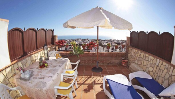 Un patio con una mesa lista para dos personas, una sombrilla y sillones de descanso.