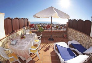 Un patio con una mesa lista para dos personas, una sombrilla y sillones de descanso.