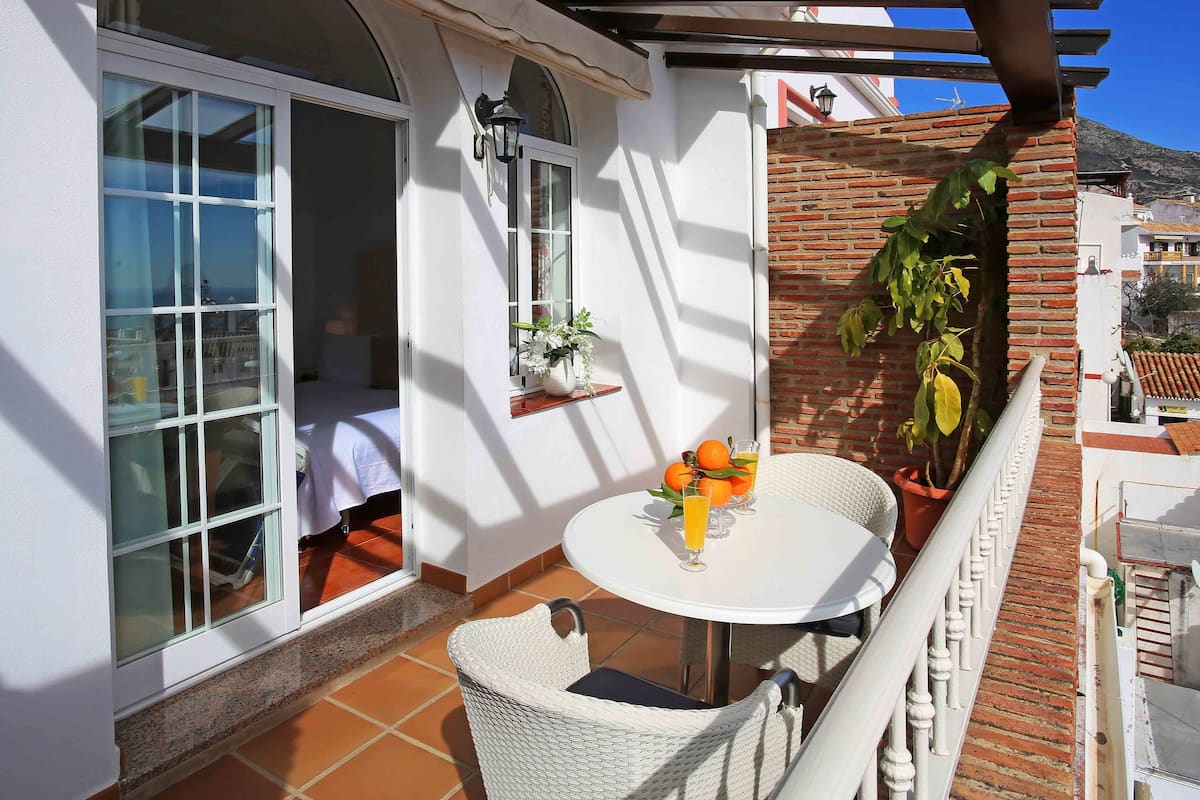 A balcony with a white table, chairs, and a potted plant.