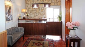 Una sala de estar con sofá, alfombra, mesa de centro de madera, pared de piedra, zona de cocina con mostrador y puerta de madera.