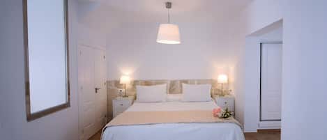 A bedroom with a large bed, two bedside tables with lamps, a stone accent wall, and a wooden floor.