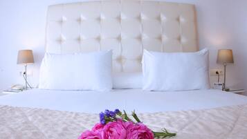A hotel room with a tufted headboard, white bedding, two bedside lamps, and a bouquet of pink and purple flowers on the bed.