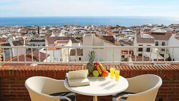 Una terraza con dos sillas de mimbre, una mesa, un frutero y un vaso de zumo de naranja.