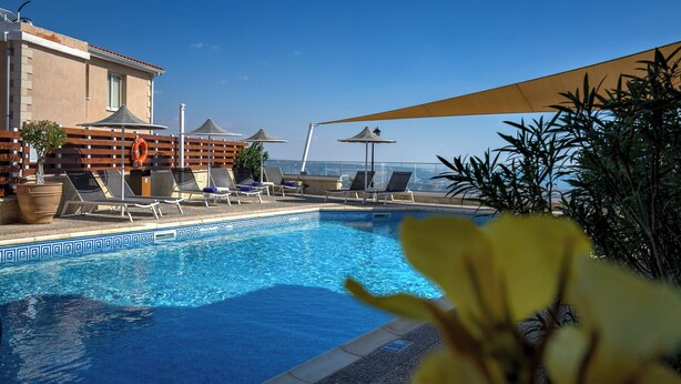 A pool area with lounge chairs and umbrellas, a clear blue sky, and a building with a tiled pool edge. - Hill View Restaurant & Apartments (Pissouri)